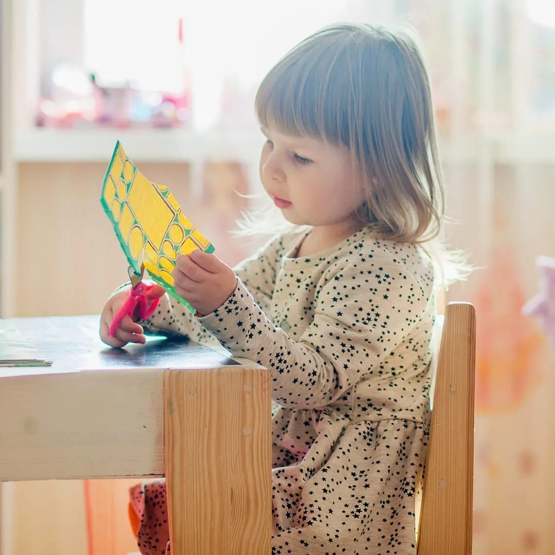 A preschooler holds up the painted paper she has been cutting.