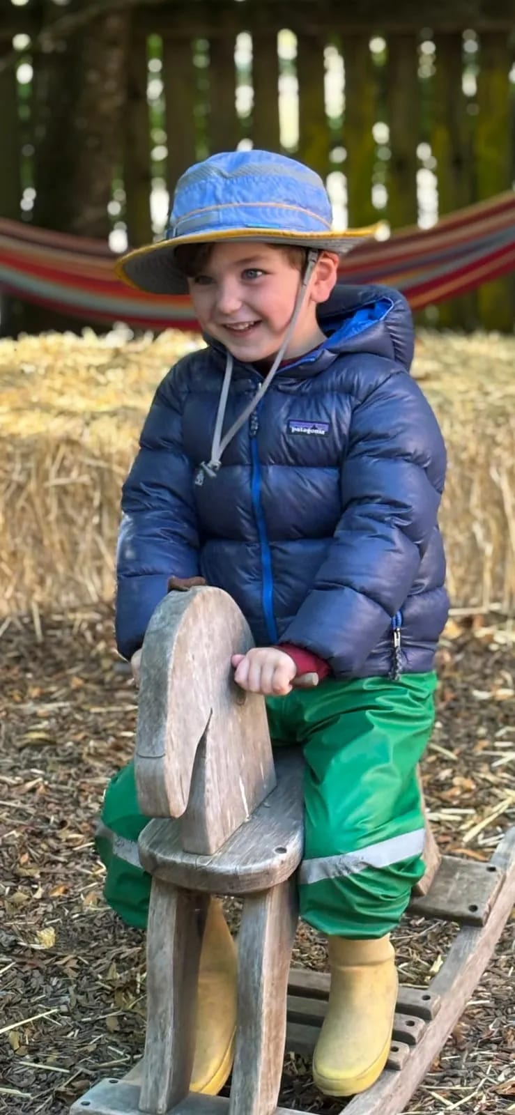 Bundled against the cold, a preschooler rides the wooden horse in the yard.
