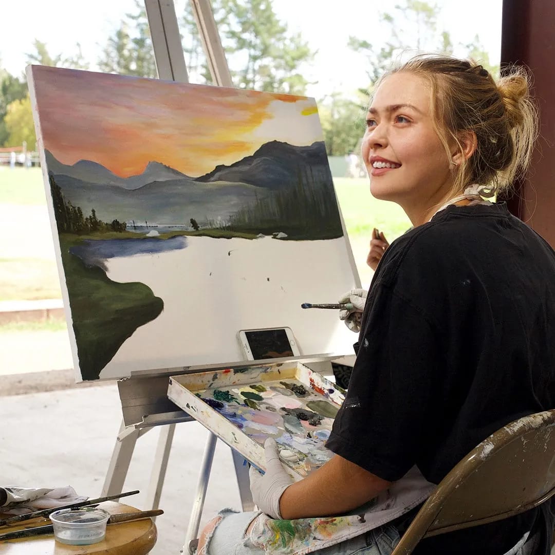 A student at the easel with her landscape in oils.