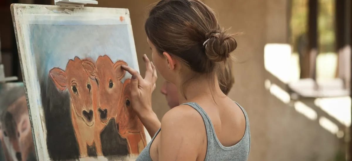 A high school student works on a pastel drawing of three calves.