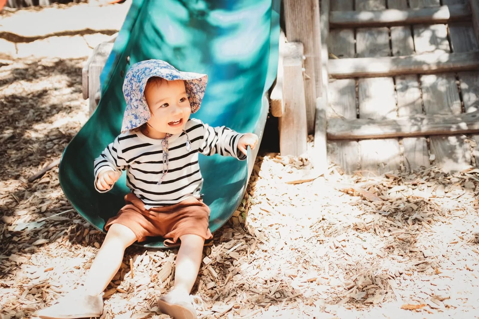 A toddler lands grinning at the bottom of the slide.